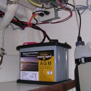 House battery beneath Wallis against aft bulkhead. GFI outlet above fed by shore power and feeds battery tender/charger and extension cord by helm station.