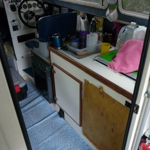 Two Bears in boating mode.  Cabinet door is now a sheet of plywood covering the under sink area.  The arm of the helm seat is off as we found it it often in the way of getting in and out of the "fridge" and of the helm seat.  This floor covering is now gone. We have gone to carpet runner floor covering (from our local hardware store) and change it yearly.  Just visible behind and to right of the helm seat are several "pockets" held to wall with Velcro.  They hold keys, wallet, & misc small items.
