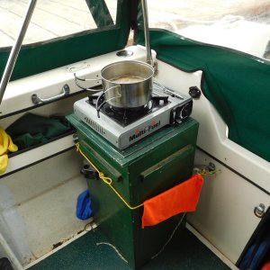 Outside Cooking.
Built box to hold stove on top for cooking and inside for travel.  Also holds fuel & many other bits of gear.  Rope holds  in place when trailering.  Note "D" rings mounted around inside  of cockpit to tie in gear.  Black 6 sided thing near front corner of stove is cap over 12 volt electric inlet/ outlet for line from tow vehicle  to power house battery when trailering or to provide 12 volt power in cockpit.