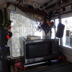 Microwave,  hanging by the door, emergency gear, flashlights, knife, multiple tool.  Strobe lights, whistle.  Window covers roll out next to wooden valance.  In back ground one of the extra fuel cans for generator held captive by SS tube across the splash well.