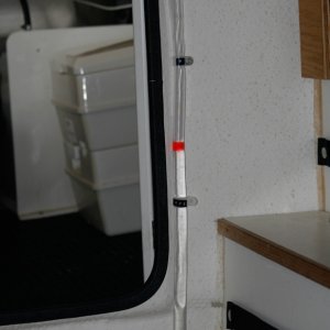 Water Tank Sight Tube added to allow quick monitoring of water level in tank inside port storage enclosure. Black label tape on the tube clamps mark 1/2 and Full Levels. One end of the tube tees into the 1/2 inch tube exiting the bottom of the tank and the other end tees back into the vent tube exiting the top of the tank. I got the idea of a colored ball or float from Sea Wolf (thanks, Joe).