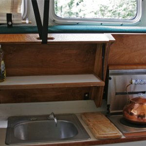 Media 'Galley with helm seat still down.' in album 'Covers are raised and helm seat pivots up to use galley. Hot items can be placed on ceramic tiles under helm seat. Small drop-down shelf inside forward cover is made of starboard trimmed in teak. Snap on elastic bands are handy for holding essentials (spelled COFFEE press) when underway.'