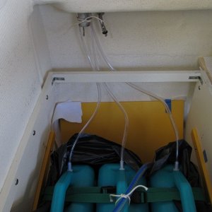 Ran hoses up to currently unused water fill (just to have a place to gather them, nothing to do with the fill in particular), and then with a piece o string tied them in place.  The hose compresses slightly so stays there. I also decided to put the jugs into a contractor bag just as a sort of liner in case there are drips when I'm filling or etc.