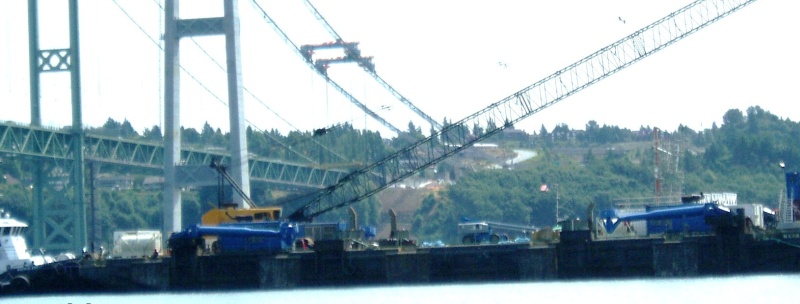Bad photo, sorry. Barge that will move road deck piece under gantry cranes. Notice huge blue 750 hp thruster motors that will help keep the barge in place using a GPS system. A tug will also be used. 
The thrusters are shown here in the up position.