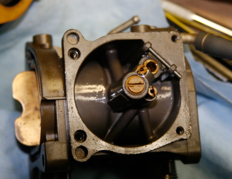 Carb-viewed-from-bottom-with bowl-cover-removed: Below brass cap screw in center lies main nozzle and emulsifier tube (slow jet). Two other jets unscrew for inspection and cleaning. Float has been removed.