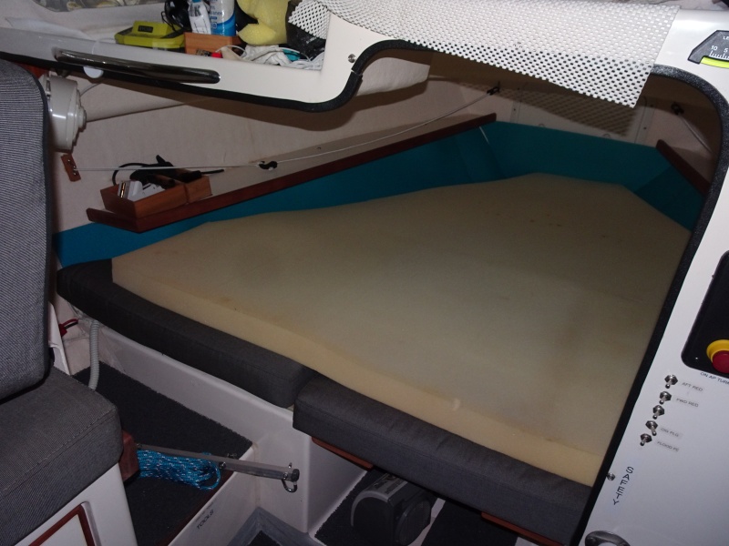 port bulkhead removed to open up the V berth.  Note 4" memory foam pad on top for comfort!  We have also put pads on the side of the bunk and under the bunk to eliminate any condensation there.  There is a teak grab rail on the upper forward area under the windshield.  In back of that is another dual outlet USB charger.  There ia the Maestro fan in the outboard part of the aft part of the V berth.  The control for this (speed, light --white or red) is located just inside on the overhead.  The fan is easily adjusted from either in the bunk or from outside.  Same for the other side.  
The cutout opens up the cabin, and makes entry into the bunk much easier.