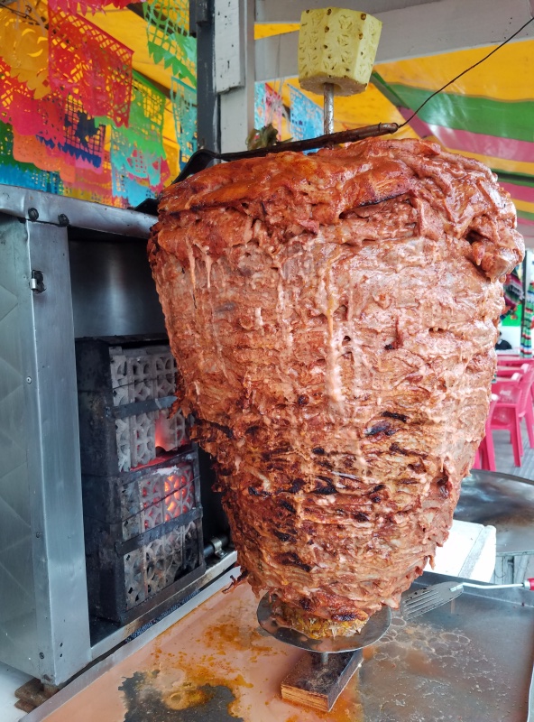 Thin layers of marinated pork stacked on a spit then slowly rotated in front of the flames, then thinly sliced off for \"al Pastor\" street tacos, so good!