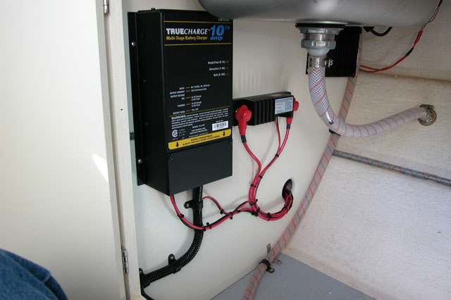 True Charge 10 Amp battery charger mounted under galley on front bulkhead on the left, Blue Sea Systems CL-Series BatteryLink a battery combiner on the right