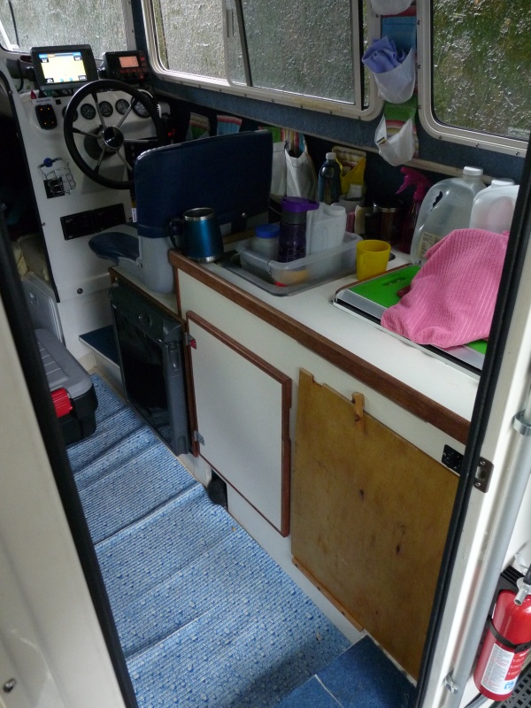 Two Bears in boating mode.  Cabinet door is now a sheet of plywood covering the under sink area.  The arm of the helm seat is off as we found it it often in the way of getting in and out of the "fridge" and of the helm seat.  This floor covering is now gone. We have gone to carpet runner floor covering (from our local hardware store) and change it yearly.  Just visible behind and to right of the helm seat are several "pockets" held to wall with Velcro.  They hold keys, wallet, & misc small items.